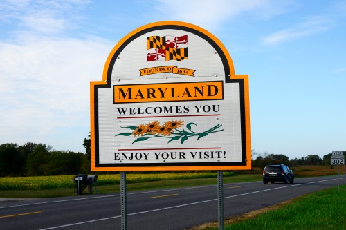 A welcome sign for Maryland featuring the state flag and the text "Maryland Welcomes You! Enjoy Your Visit!"