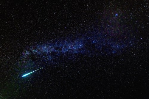 A stunning night sky filled with stars, featuring a bright meteor streaking across the Milky Way galaxy.