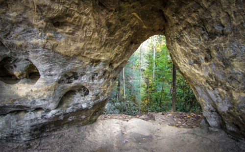 A natural rock formation with an arch, framing a view of lush green trees in the background.
