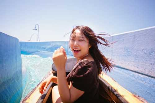 A young woman smiles joyfully while riding a water slide, with her hair blowing in the wind and water splashing around.