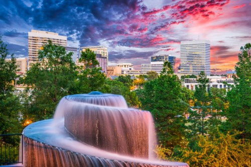 A cascading fountain in the foreground with a vibrant sunset and city skyline in the background.