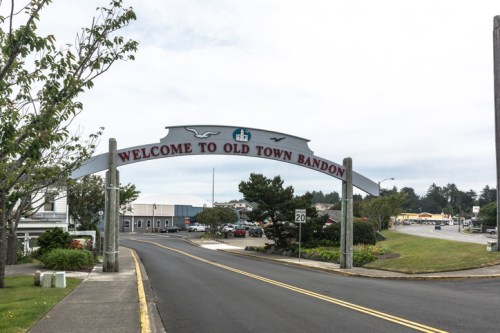 Sign welcoming visitors to Old Town Bandon, with trees and buildings in the background on a cloudy day.