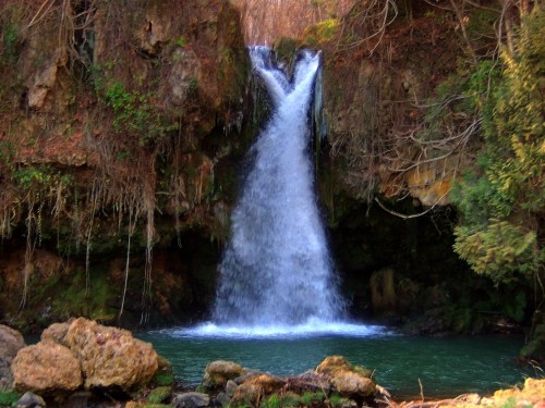 A serene waterfall cascading into a tranquil pool, surrounded by lush greenery and rocky terrain.