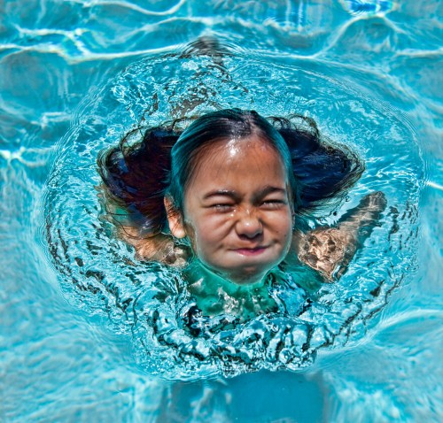 A child underwater with a playful expression, surrounded by shimmering blue water.