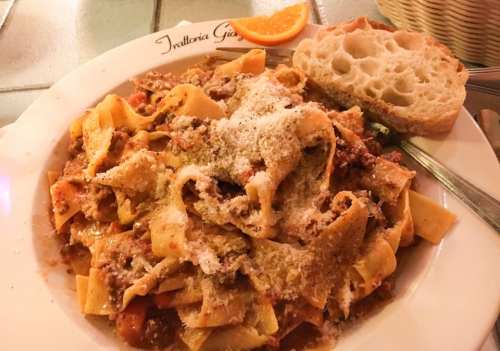 A plate of pasta with meat sauce, topped with grated cheese, served with a slice of bread and an orange wedge.