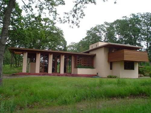 A modern house with a flat roof, large windows, and wooden accents, surrounded by greenery and trees.