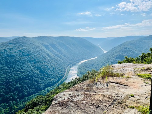 A panoramic view of a lush green valley with a winding river, framed by mountains under a clear blue sky.