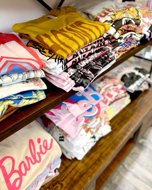 A display of neatly folded graphic t-shirts in various colors and designs on wooden shelves.