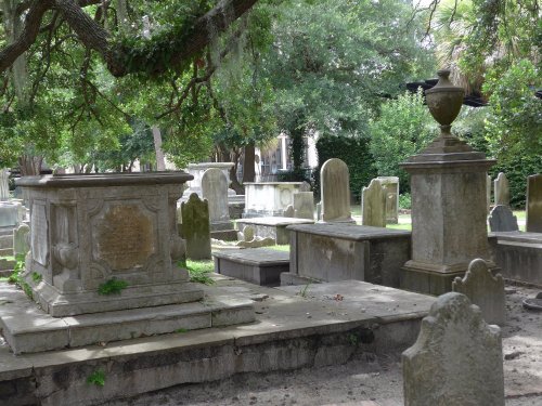 A serene cemetery scene with various gravestones and monuments surrounded by trees and greenery.