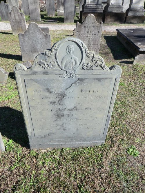 A weathered gravestone with an engraved portrait, surrounded by other gravestones in a cemetery.