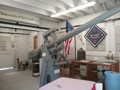 A historic cannon displayed in a museum, with an American flag and artifacts about shipwrecks in the background.