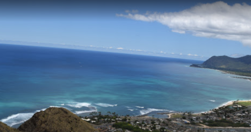 A panoramic view of a coastline with turquoise waters, sandy beaches, and mountains under a clear blue sky.