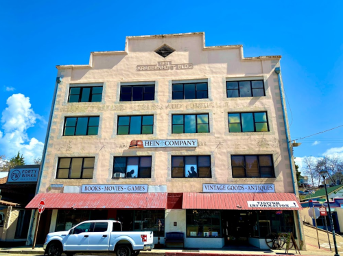 Historic building with large windows, featuring signs for a bookstore, vintage goods, and antiques. A white truck is parked outside.