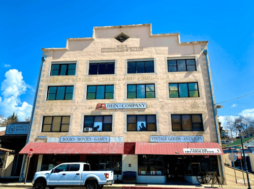 Historic building with large windows, featuring signs for a bookstore, vintage goods, and antiques. A white truck is parked outside.