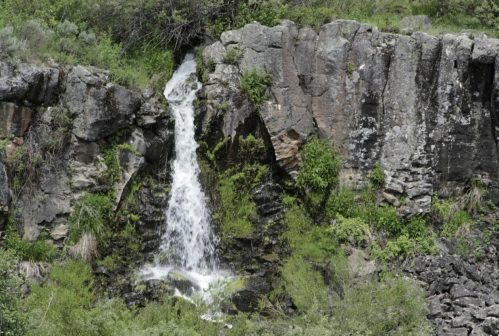 A small waterfall cascades down rocky cliffs, surrounded by lush green vegetation.