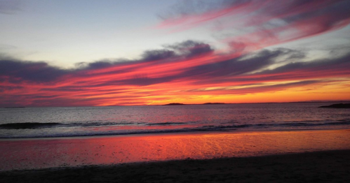 A vibrant sunset over the ocean, with colorful clouds reflecting on the water's surface.