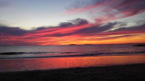 A vibrant sunset over the ocean, with pink and purple clouds reflecting on the water's surface.
