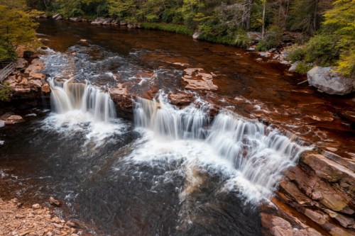 A serene river with cascading waterfalls surrounded by lush greenery and rocky banks.