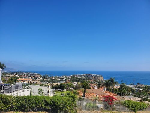 A scenic view of a coastal town with blue ocean, clear skies, and lush greenery in the foreground.
