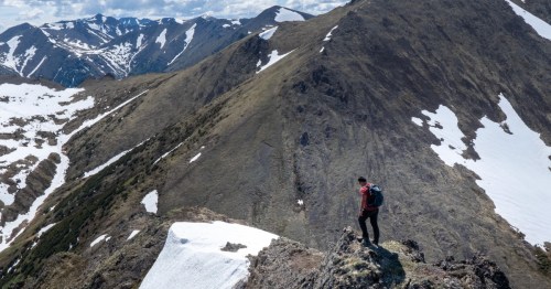 Hope Point Summit: Hiker stands on a rocky, snow-dusted ridge with rugged brown mountains stretching into the distance.