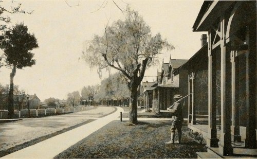 A historic street scene featuring houses, a tree, and a person standing with a tool in a quiet neighborhood.