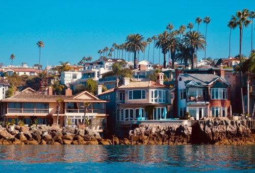 Coastal view of colorful homes along a rocky shoreline, with palm trees and clear blue skies in the background.