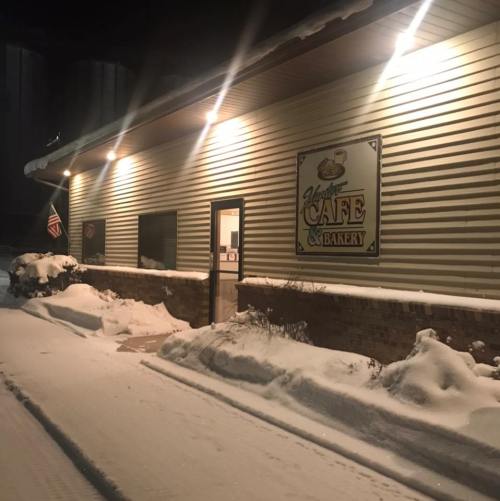 A cozy café and bakery with a sign, illuminated at night, surrounded by snow-covered ground.