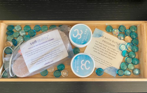 A wooden tray filled with blue gel beads, bath products, and an informational card about a bath program.