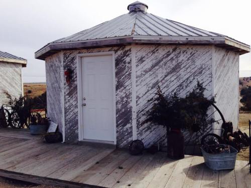 A rustic round building with a metal roof, wooden deck, and decorative items, set against a vast landscape.