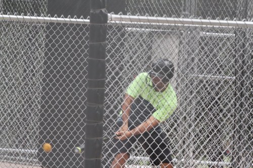 A person in a neon green shirt swings a bat in a batting cage, with a ball approaching.