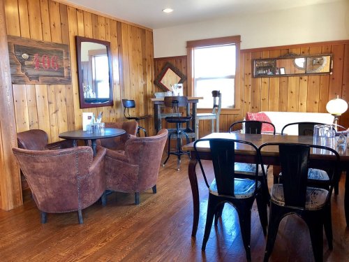 Cozy interior of a rustic café with wooden walls, tables, and chairs, featuring a mirror and decorative accents.