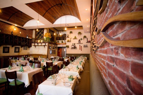 Interior of a cozy restaurant featuring brick walls, wooden accents, and neatly set tables with green napkins.