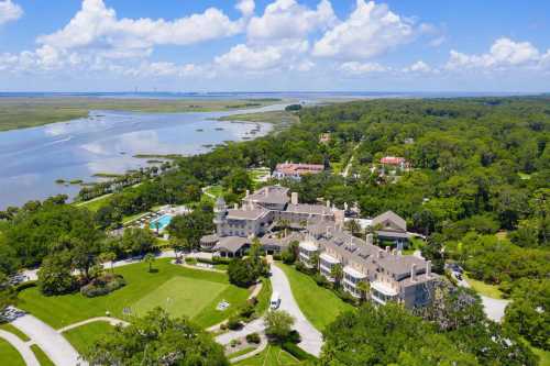 Aerial view of a large estate surrounded by lush greenery and water, with a pool and landscaped grounds.