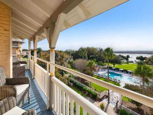 A balcony view overlooking a pool and lush landscape with palm trees and a river in the distance.