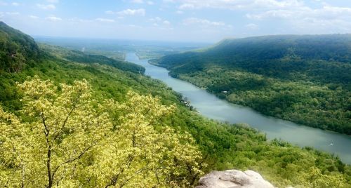 A scenic view of a lush green valley with a winding river under a blue sky with fluffy clouds.