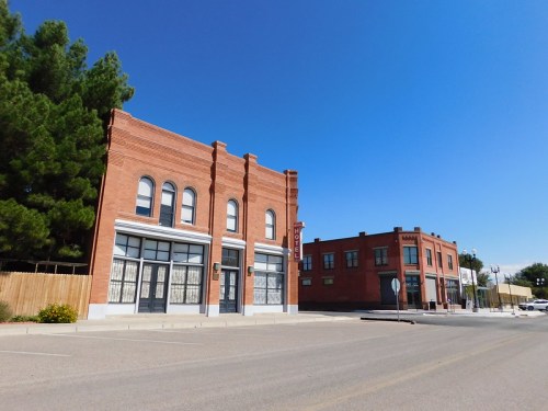 Historic brick buildings line a quiet street under a clear blue sky, with trees in the background.