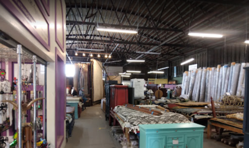 A spacious warehouse filled with various furniture and decor items, illuminated by overhead lights.