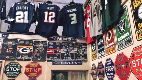 A wall displaying sports jerseys and various team signs, featuring NFL teams like the Patriots, Packers, and Ravens.