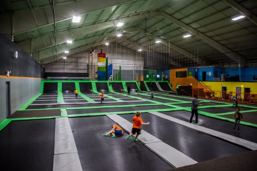 A spacious indoor trampoline park with kids jumping and playing on green and black trampolines.