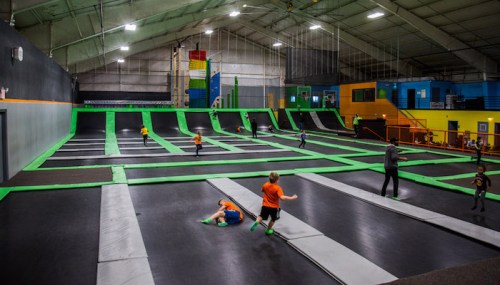 A spacious indoor trampoline park with kids jumping and playing on multiple trampolines surrounded by colorful walls.