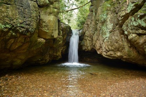 A serene waterfall cascades into a clear pool, surrounded by rocky cliffs and lush greenery.