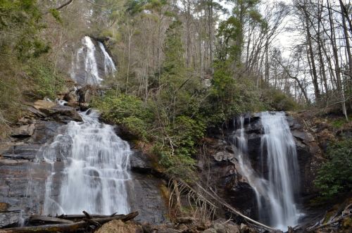 Two cascading waterfalls surrounded by lush greenery and rocky terrain in a serene forest setting.