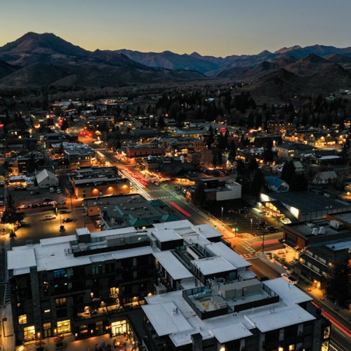 Aerial view of a town at dusk, with mountains in the background and streets illuminated by city lights.