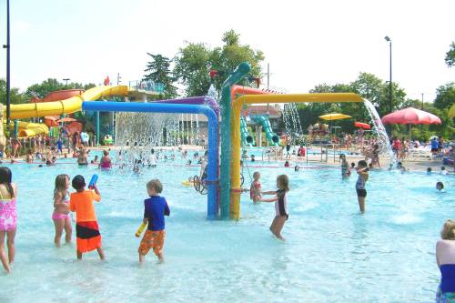 Children playing in a water park with colorful slides and splash features on a sunny day.