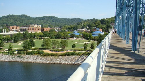 View from a bridge overlooking a park and river, with hills and buildings in the background.