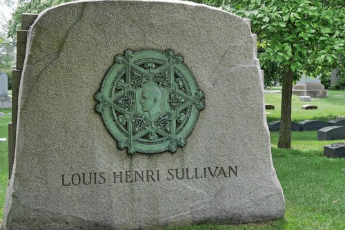 Gravestone of Louis Henri Sullivan featuring a decorative emblem and surrounded by green grass and trees.