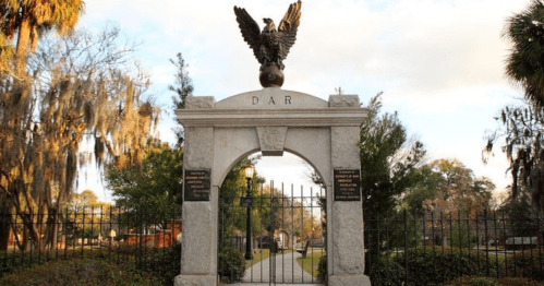 Stone archway with an eagle atop, featuring "DAR" and plaques, surrounded by trees and a gated entrance.