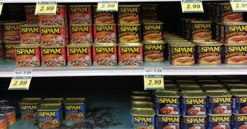 A grocery shelf displaying various cans of Spam, including different flavors and sizes, with price tags visible.