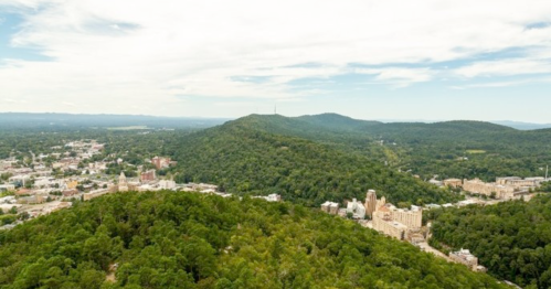 Aerial view of a lush green landscape with hills and a small town nestled below under a partly cloudy sky.