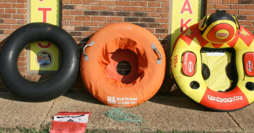 Three inflatable tubes in various colors and sizes are displayed against a brick wall, with a small red flag nearby.